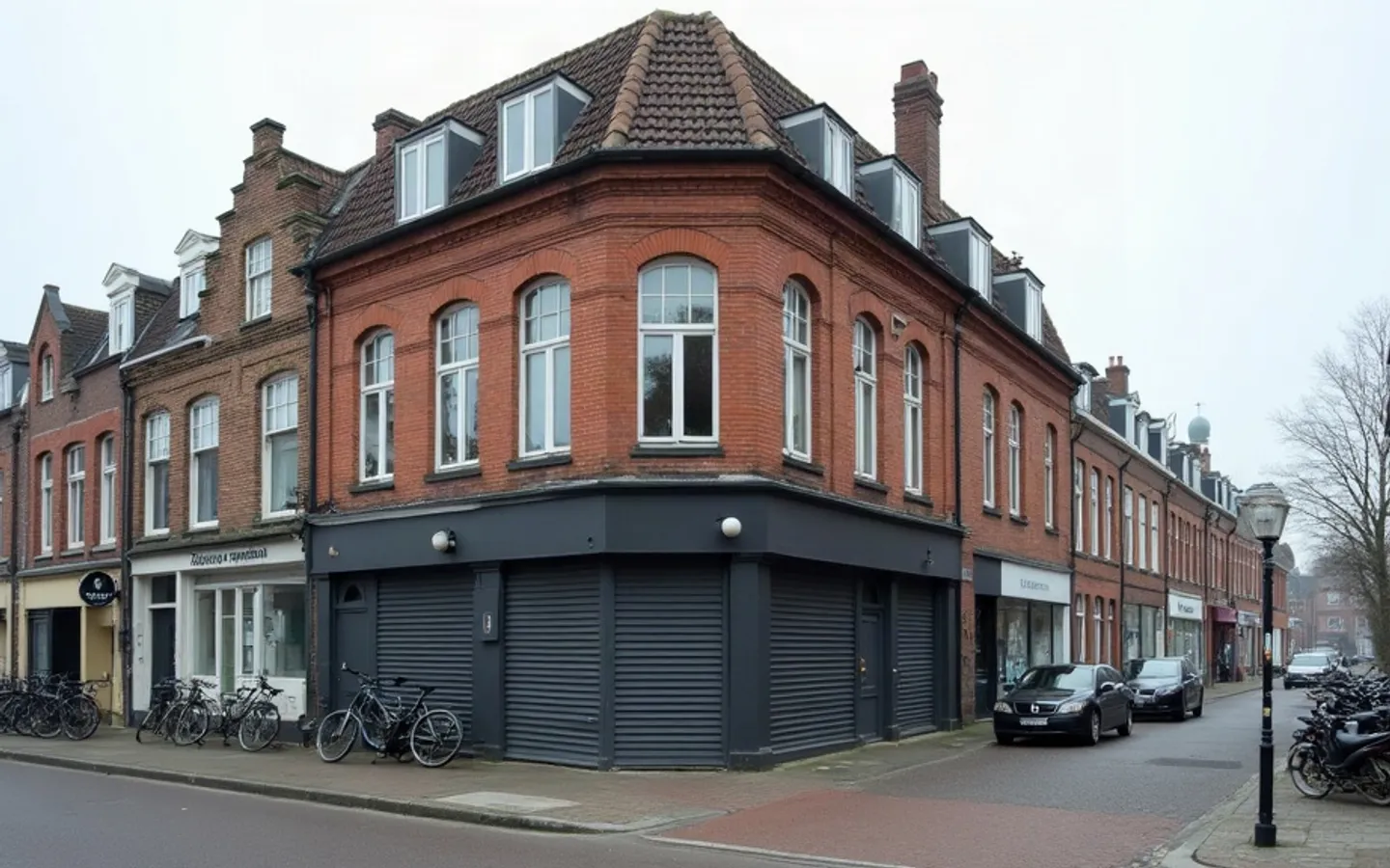 Rij bakstenen woningen aan een rustige straat in ochtendlicht, met bij één portiek meerdere brievenbussen en deurbellen naast elkaar.