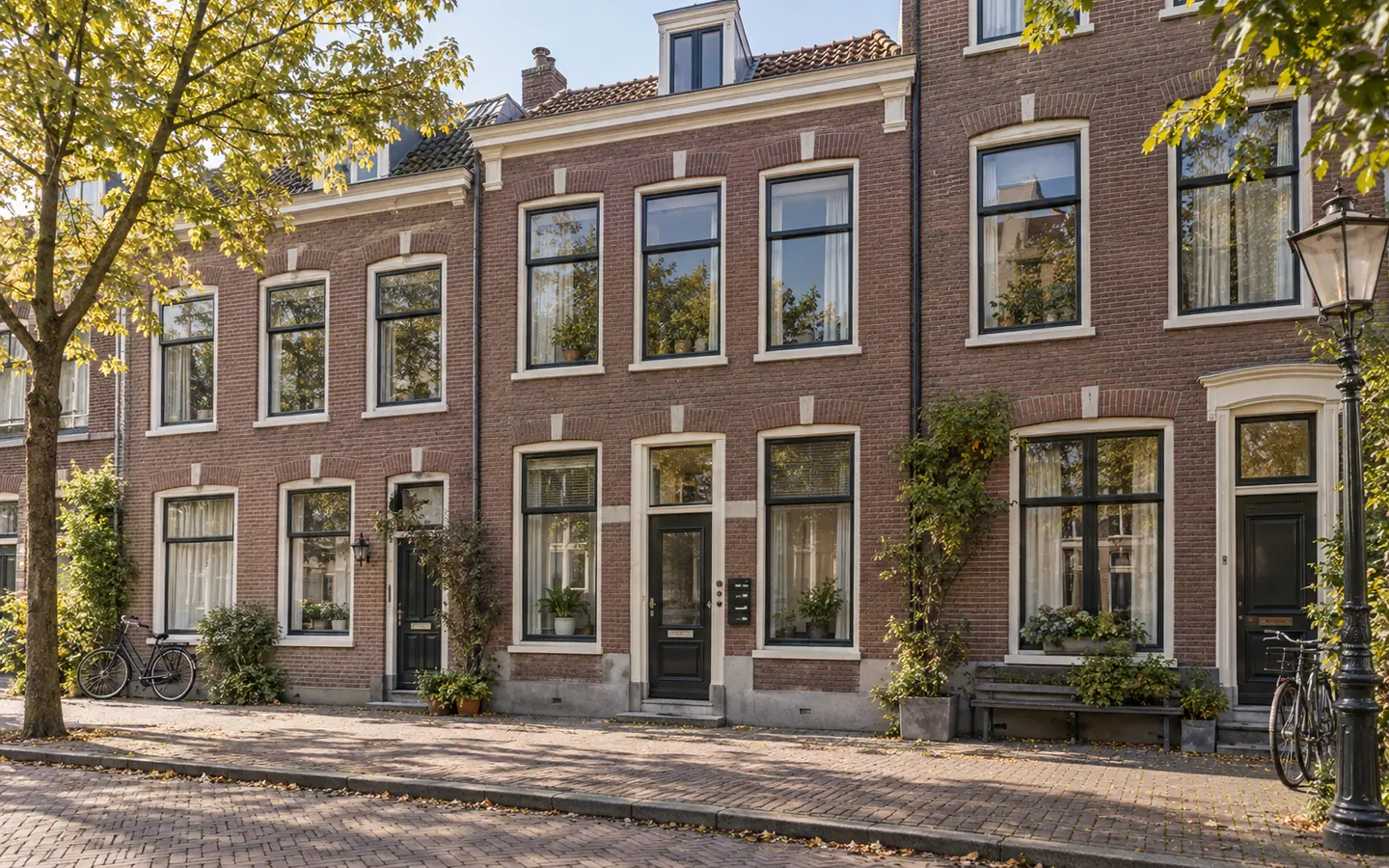 Rij bakstenen woningen aan een rustige straat in ochtendlicht, met bij één portiek meerdere brievenbussen en deurbellen naast elkaar.
