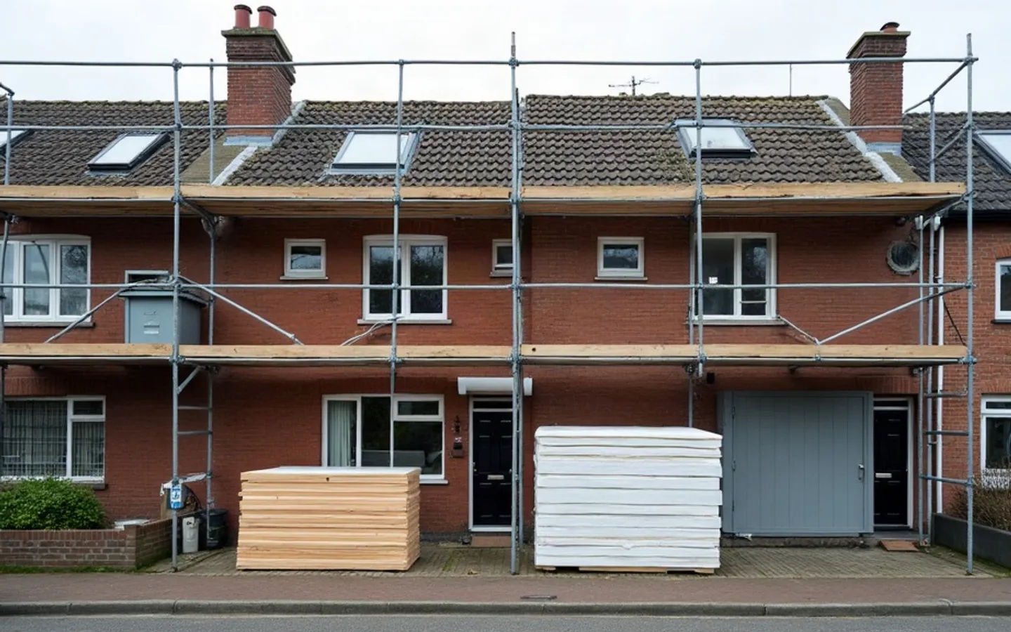 Rij vooroorlogse bakstenen bovenwoningen in ochtendlicht, waarvan één gevel in de steigers staat met nieuwe isolatieplaten en de andere gevels onaangeroerd zijn.